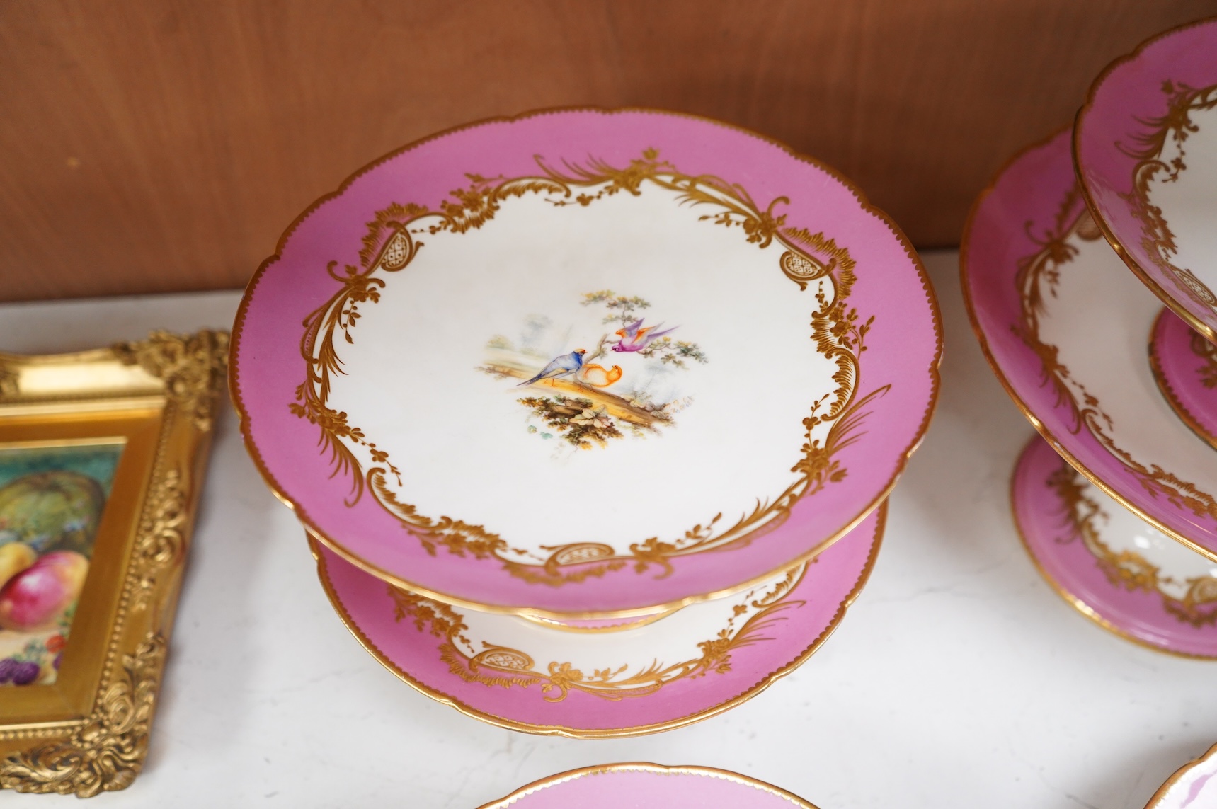A Minton pink ground dessert service, in Sevres style, c.1850, hand painted with birds, comprising four comports and ten dessert plates, 23cm in diameter